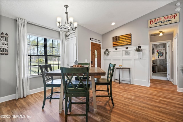 dining area featuring a chandelier, vaulted ceiling, wood finished floors, a decorative wall, and a textured ceiling