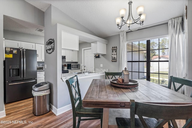 dining room with baseboards, lofted ceiling, wood finished floors, a notable chandelier, and a textured ceiling