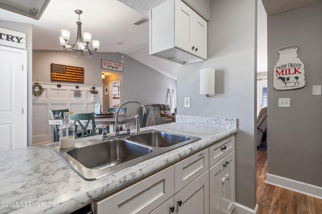 kitchen featuring visible vents, a sink, dark wood finished floors, white cabinetry, and vaulted ceiling