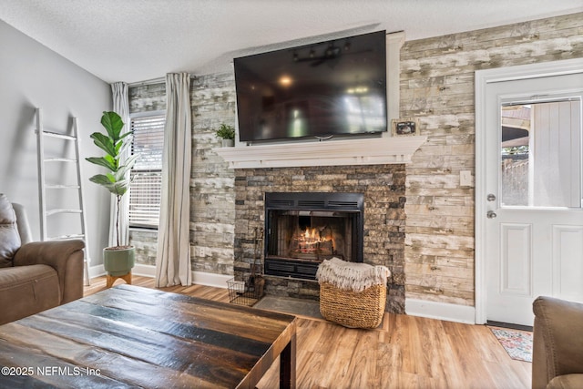 living room with a wealth of natural light, a stone fireplace, a textured ceiling, and wood finished floors