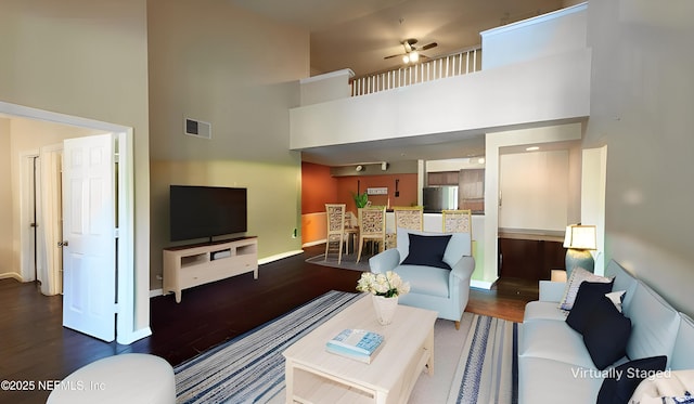 living room with visible vents, baseboards, wood finished floors, and a towering ceiling