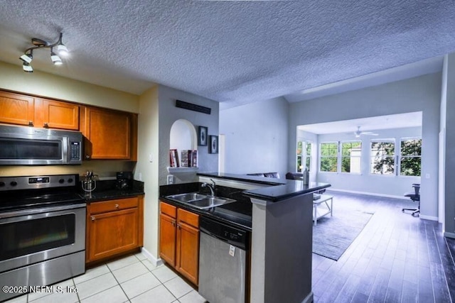 kitchen featuring a peninsula, a sink, appliances with stainless steel finishes, dark countertops, and open floor plan