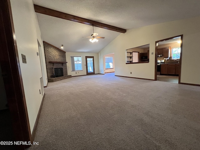 unfurnished living room with a ceiling fan, vaulted ceiling with beams, a textured ceiling, a brick fireplace, and light colored carpet