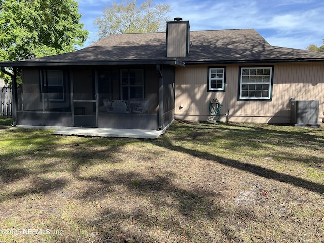 rear view of house with roof with shingles, a lawn, cooling unit, a chimney, and a sunroom