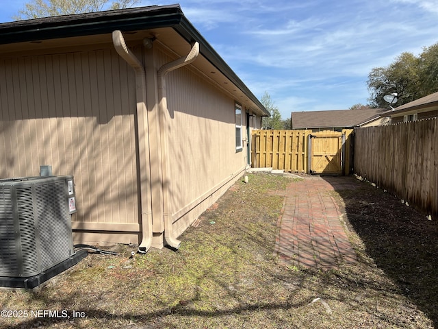 view of property exterior with fence, central AC, and a gate