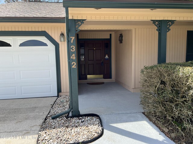 view of exterior entry with an attached garage and a shingled roof