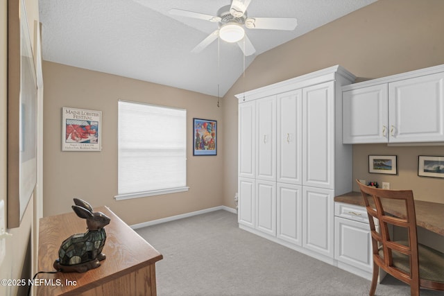 office featuring baseboards, light colored carpet, lofted ceiling, a textured ceiling, and a ceiling fan