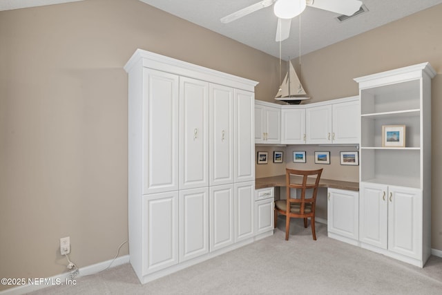 kitchen with dark countertops, built in study area, ceiling fan, light colored carpet, and white cabinetry