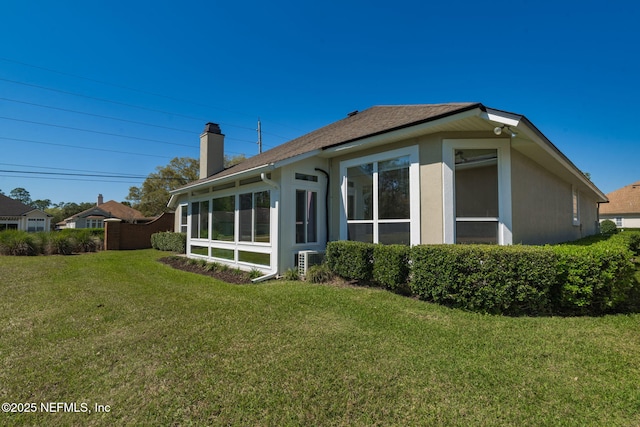 back of house with a yard, a chimney, a sunroom, and stucco siding