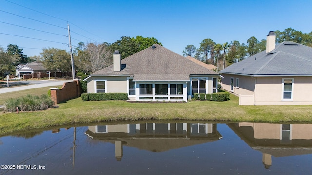 back of house featuring a yard, a water view, roof with shingles, and stucco siding