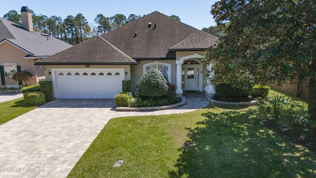 view of front of house with roof with shingles, driveway, an attached garage, stucco siding, and a front lawn