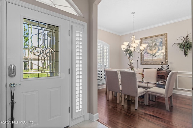 foyer with crown molding, a notable chandelier, wood finished floors, and a wainscoted wall