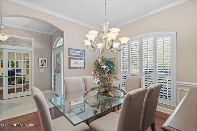 dining area featuring baseboards, ornamental molding, wood finished floors, arched walkways, and a notable chandelier