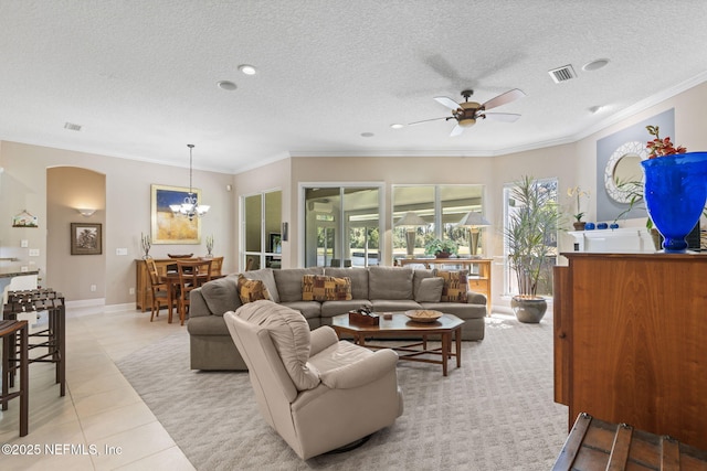 living area featuring light tile patterned floors, visible vents, a textured ceiling, crown molding, and ceiling fan with notable chandelier