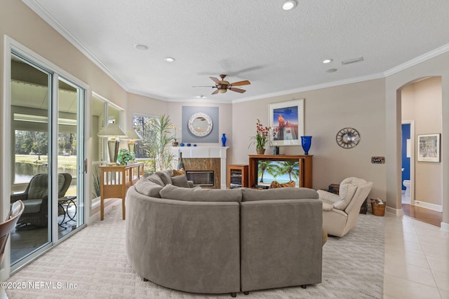 living room with a premium fireplace, light tile patterned floors, ornamental molding, arched walkways, and a ceiling fan