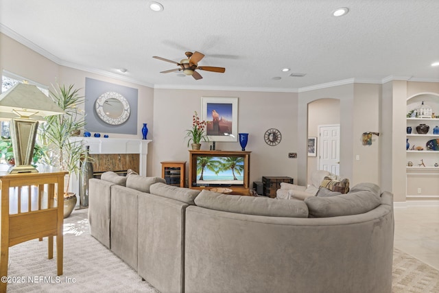 living room featuring arched walkways, a fireplace, a ceiling fan, and crown molding