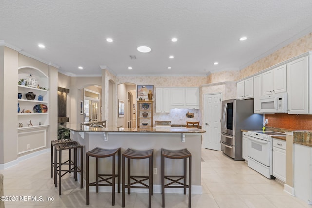 kitchen with ornamental molding, a kitchen breakfast bar, white cabinetry, white appliances, and arched walkways