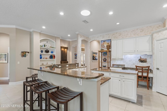 kitchen featuring visible vents, arched walkways, a breakfast bar area, and a large island with sink