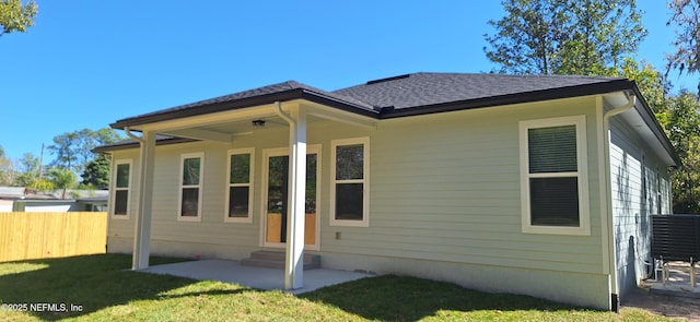 rear view of house with entry steps, fence, a yard, roof with shingles, and a patio area