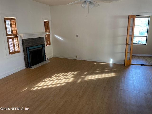 unfurnished living room featuring a ceiling fan, a fireplace with flush hearth, wood finished floors, and baseboards