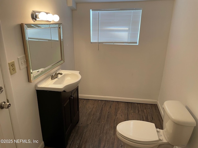 half bath featuring toilet, vanity, baseboards, and wood finished floors