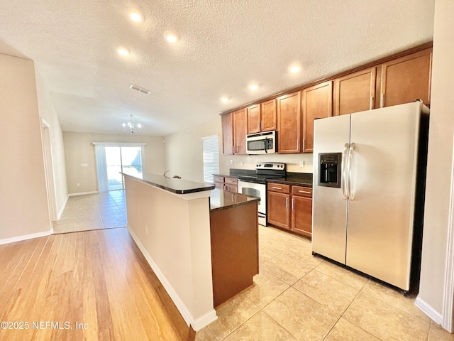 kitchen featuring dark countertops, brown cabinets, appliances with stainless steel finishes, and an island with sink