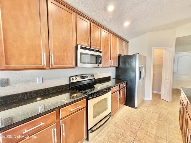 kitchen with dark stone countertops, a textured ceiling, stainless steel appliances, brown cabinetry, and lofted ceiling