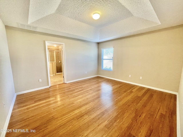 unfurnished room with a tray ceiling, light wood-type flooring, baseboards, and a textured ceiling