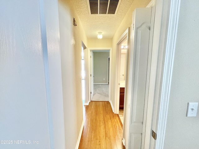 hall with baseboards, visible vents, a textured ceiling, and light wood-style floors