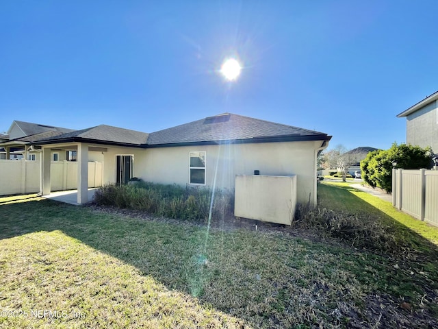 back of property with a yard, fence, roof with shingles, and stucco siding