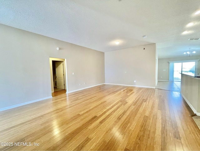 spare room with light wood finished floors, visible vents, baseboards, an inviting chandelier, and a textured ceiling