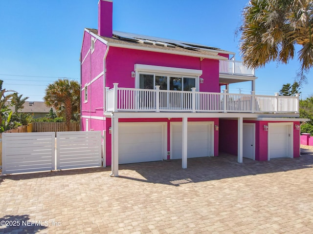 view of front of house featuring a balcony, fence, an attached garage, a chimney, and decorative driveway