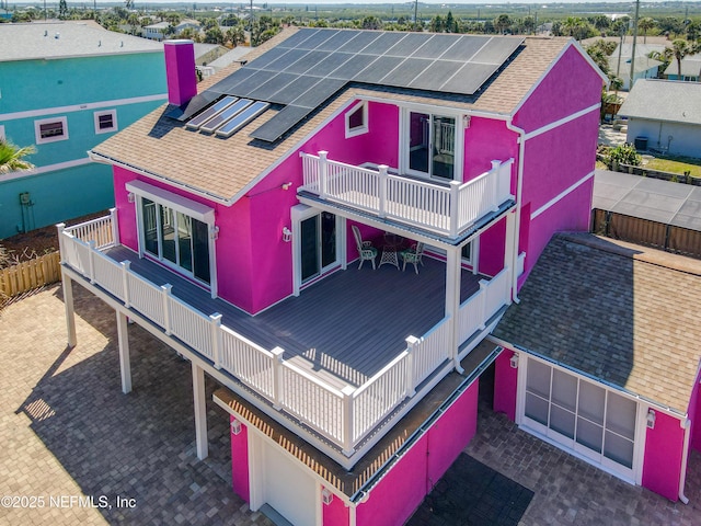 back of property with a garage, roof mounted solar panels, a balcony, and a shingled roof