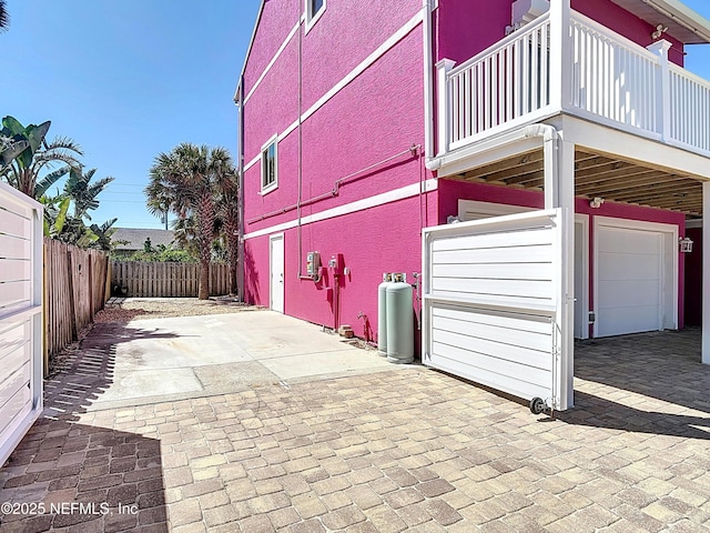 view of property exterior with a garage, brick siding, a patio area, and fence