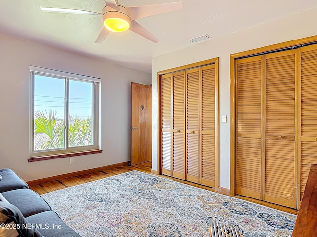 bedroom with visible vents, two closets, baseboards, and wood finished floors