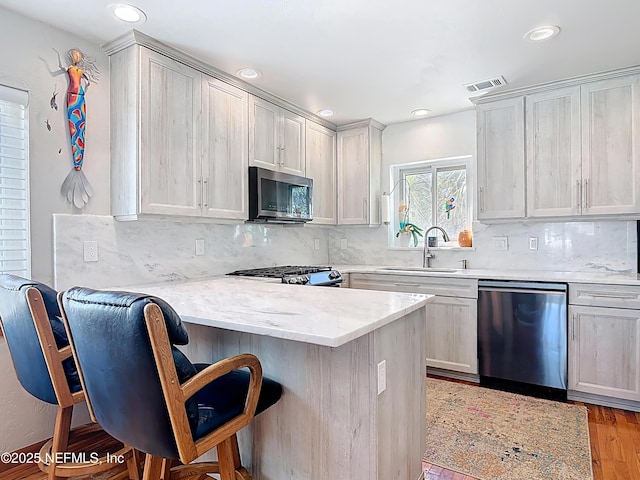 kitchen featuring visible vents, a breakfast bar, a peninsula, a sink, and appliances with stainless steel finishes