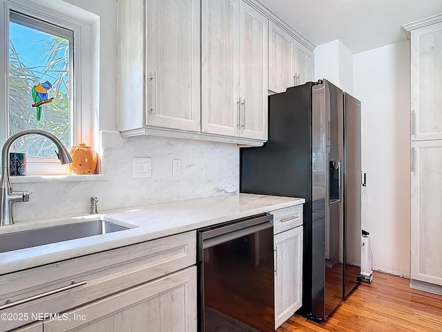 kitchen featuring light stone counters, a sink, light wood-style floors, dishwasher, and stainless steel fridge