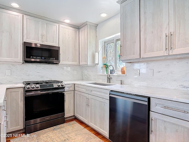 kitchen featuring light wood-style flooring, a sink, tasteful backsplash, appliances with stainless steel finishes, and light stone countertops