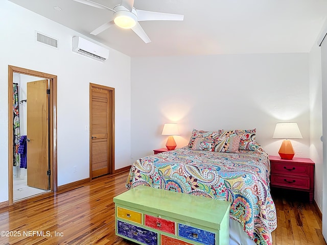 bedroom featuring visible vents, baseboards, a wall mounted air conditioner, wood finished floors, and a ceiling fan