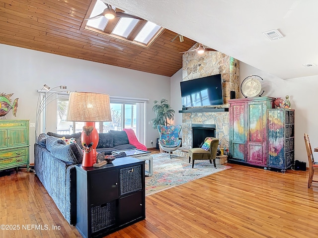 living area featuring visible vents, lofted ceiling with skylight, a stone fireplace, wooden ceiling, and wood finished floors