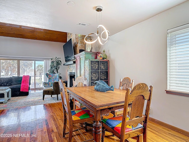 dining room featuring visible vents, a large fireplace, and light wood-style flooring