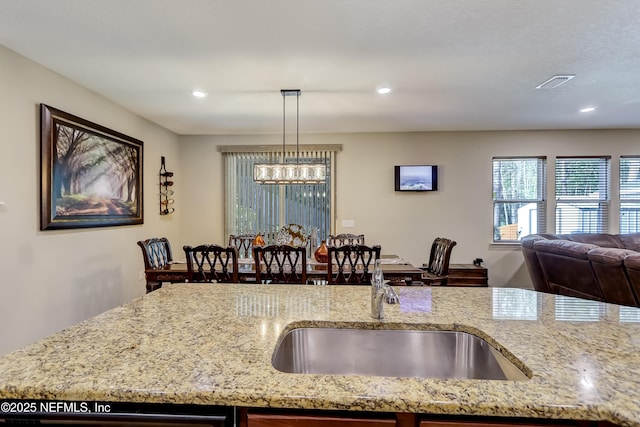 kitchen featuring a sink, light stone countertops, pendant lighting, and open floor plan