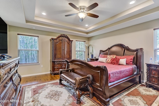 bedroom with a ceiling fan, a tray ceiling, wood finished floors, recessed lighting, and baseboards