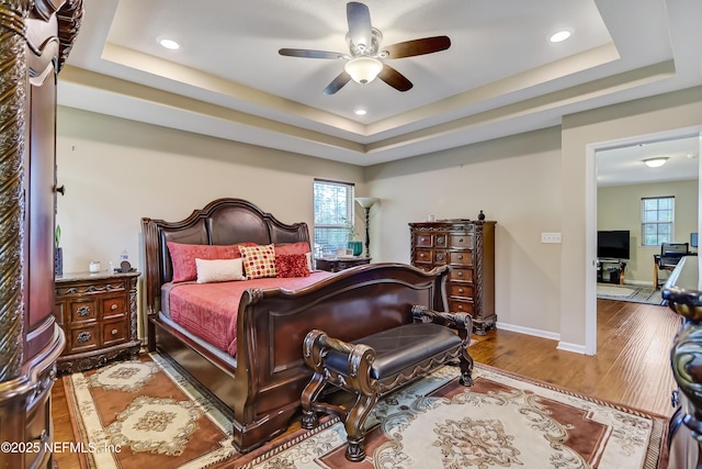 bedroom with a raised ceiling, a ceiling fan, wood finished floors, recessed lighting, and baseboards