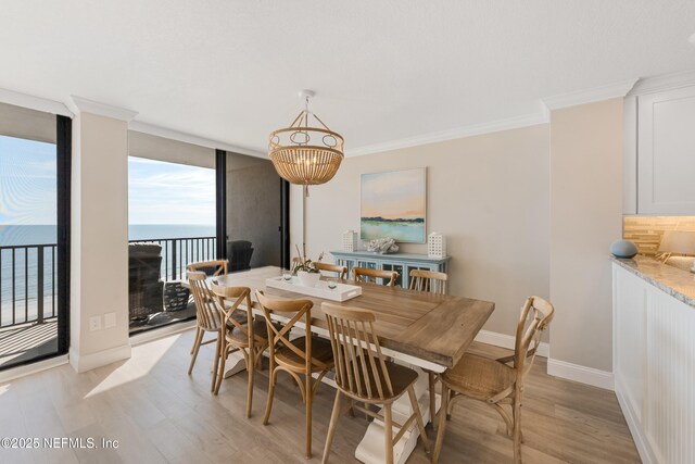 dining space with a water view, ornamental molding, light wood finished floors, a wall of windows, and baseboards