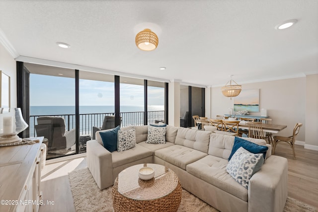 living area with light wood-type flooring, a water view, floor to ceiling windows, crown molding, and baseboards