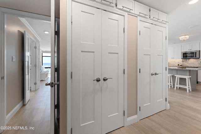 hall featuring recessed lighting, baseboards, light wood-style flooring, and crown molding