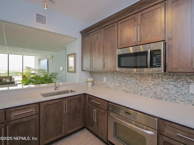 kitchen featuring a sink, decorative backsplash, light countertops, dark brown cabinetry, and stainless steel appliances