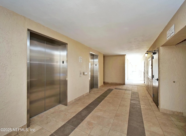 hall featuring elevator, light tile patterned flooring, and a textured wall