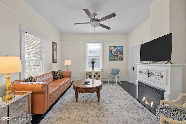 living room with a glass covered fireplace, baseboards, ceiling fan, and wood finished floors